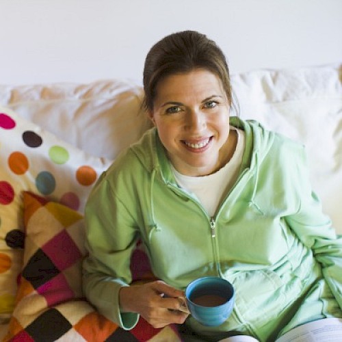 Smiling woamn relaxing on sofa with polka dot cushion and cup of coffee