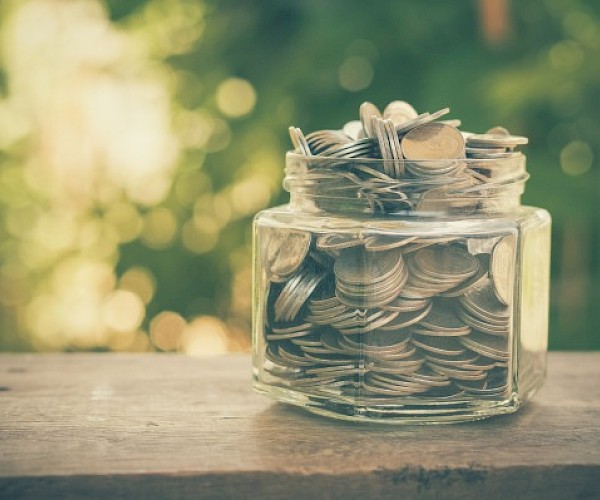 jar of money against a blurred leafy backdrop