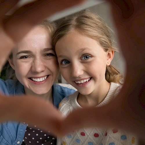 Smiling woman and girl looking through their heart shape hands to the camera