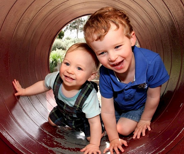 Young child and crawling baby coming out of a play tunnel a tunnel