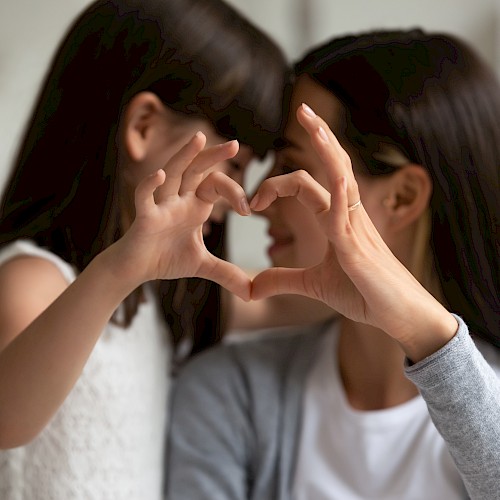 Woman and girl making a heart shape with hands to the camera