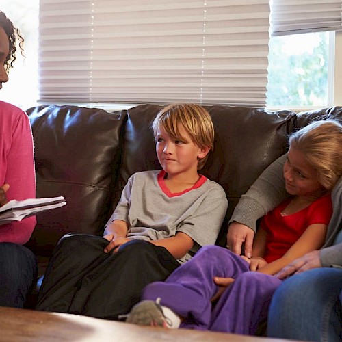Older boy and girl sitting on sofa with foster mother and chatting to lady with a notepad