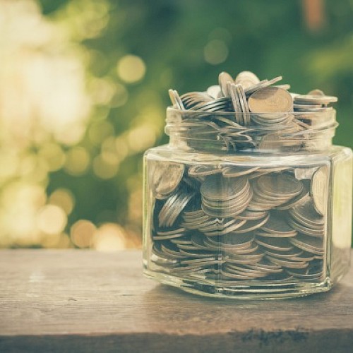 Clear jar of money against a leafy backdrop