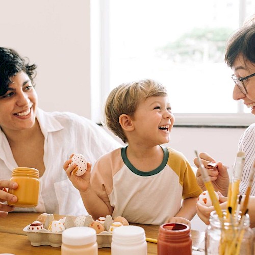 Smiling young boy, laughing with two women whilst doing crafts