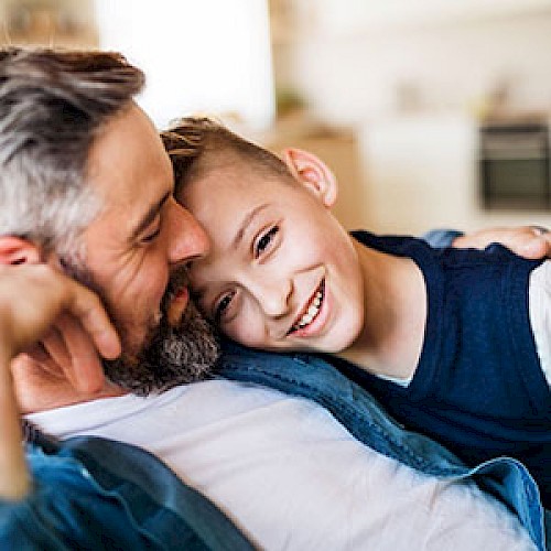 Older boy cuddling into the chest of smiling man
