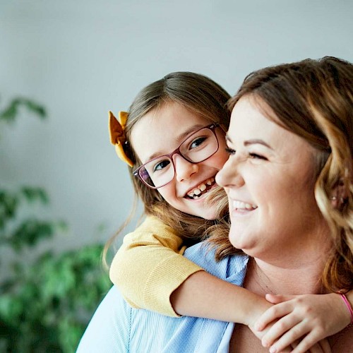 Young girl in glasses draped over the shoulder of smiling woman