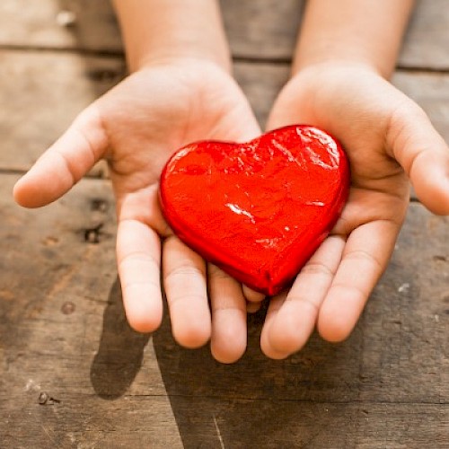 Wooden red heart in a child's hands on a wooden table top close up