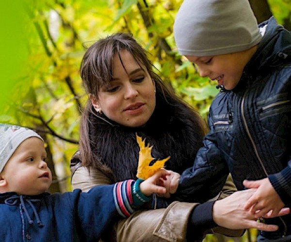 Woamn with two young children in winter coats looking at leaves