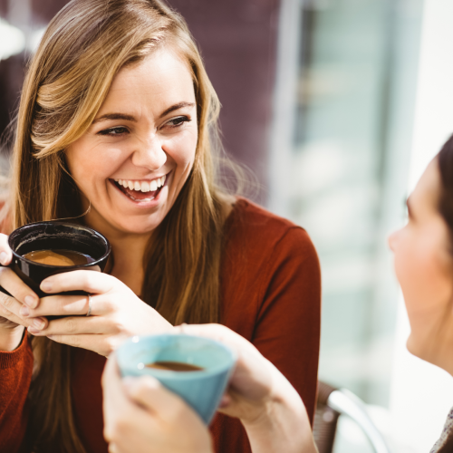 Young woman laughing with another whilst having a coffee