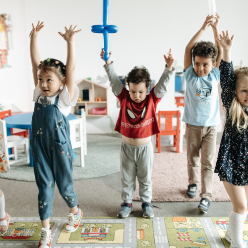 A line of small children with arms up in the air playing a game