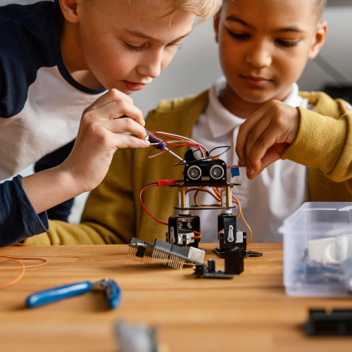 Two older boys concentrating on building a robot using wires and mechanical elements