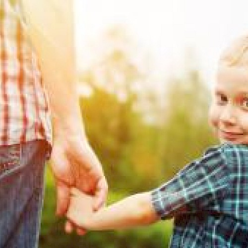 Smiling blonde boy looking over his shoulder whilst holding the hand of a man in a red checked shirt