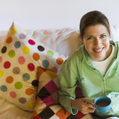 Woman relaxing on a sofa next to a polka dot cushion with a blue cup of coffee