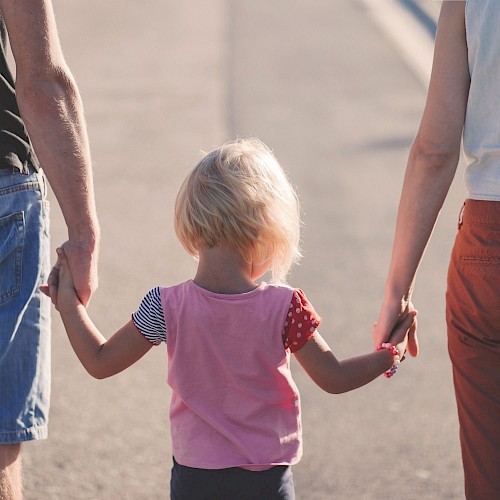 Very young blonde haired girl walking between an man and a woman holding their hands