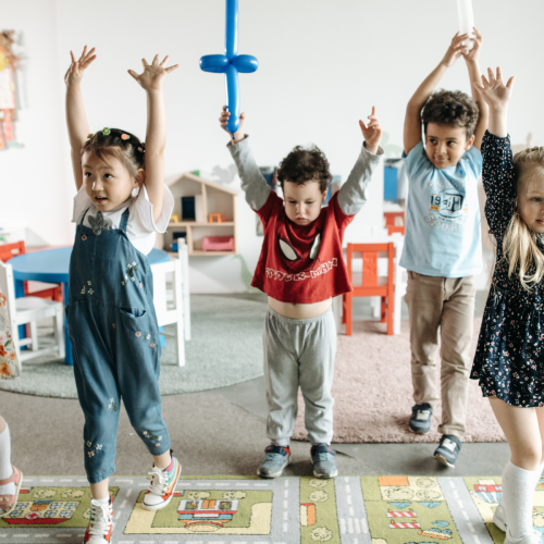 Happy young children in a playroom holding up their hands doing activities