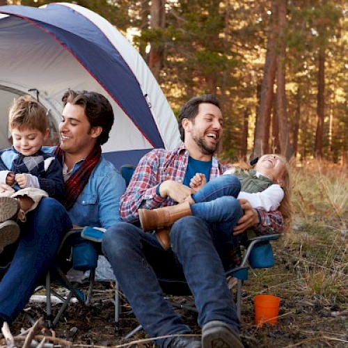 Gay male couple camping with two children laughing